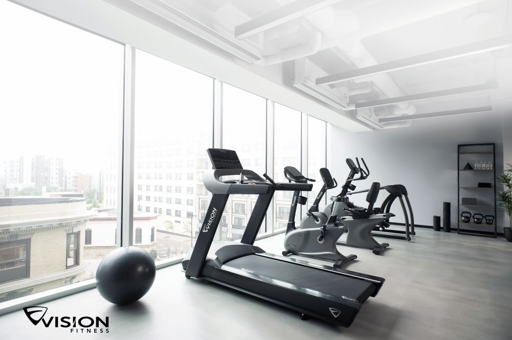 In einem Fitnessstudio sind Reihen von Ergometern und Laufbändern aufgereiht, im Hintergrund sind weitere Ergometer ordentlich gestapelt.
