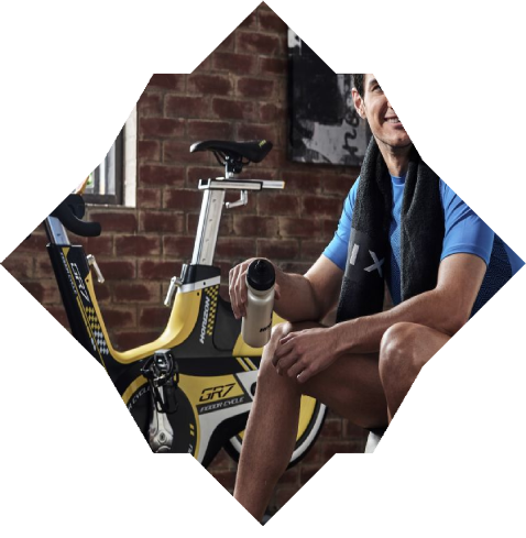 Mann ruht sich in einem Fitnessstudio aus und hält eine Trinkflasche in der Hand. Im Hintergrund ist ein Reibungswiderstand zu sehen.